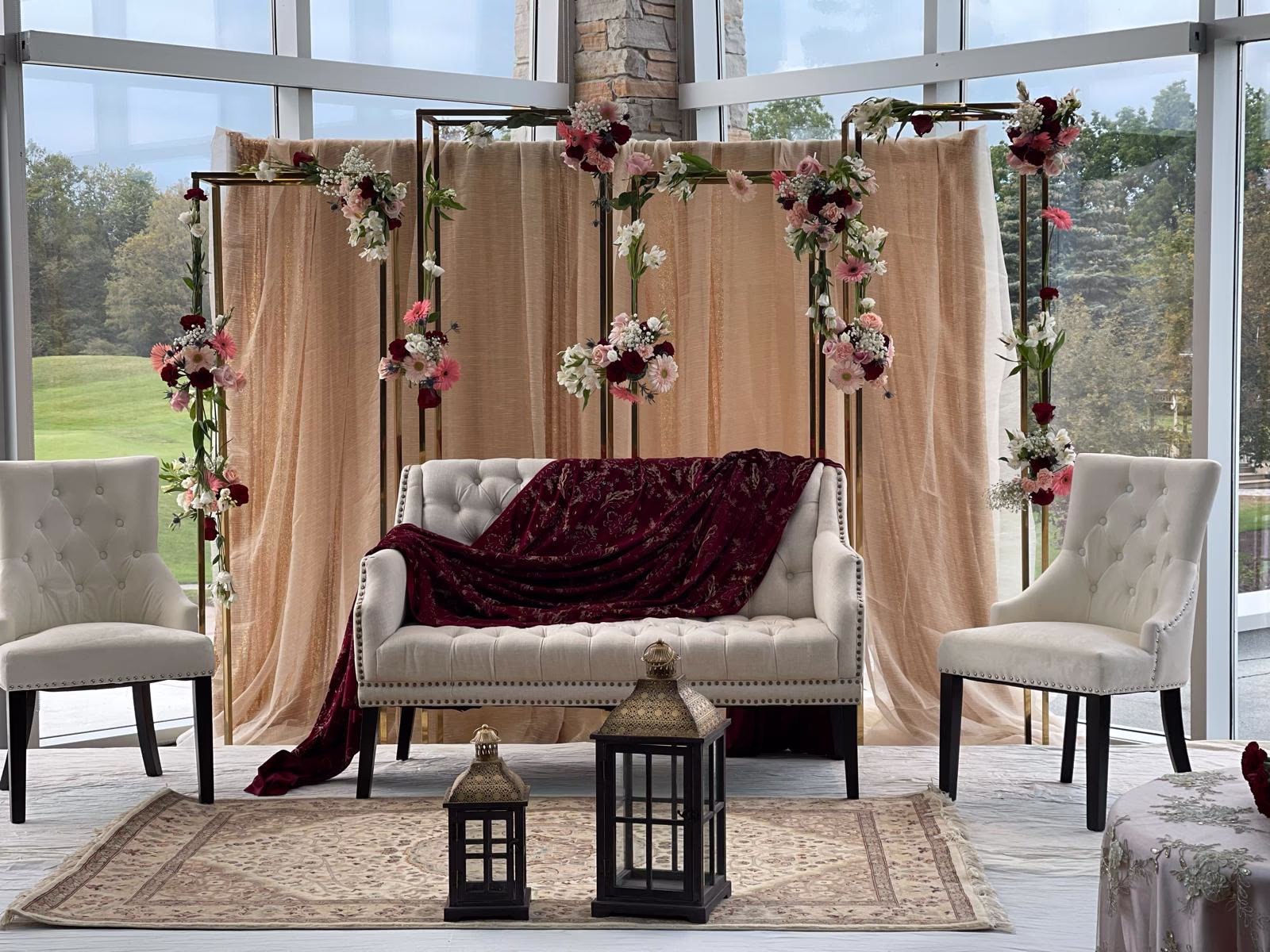 Draped ceremony lounge backdrop framed with burgundy, pink and white florals above a tufted cream settee