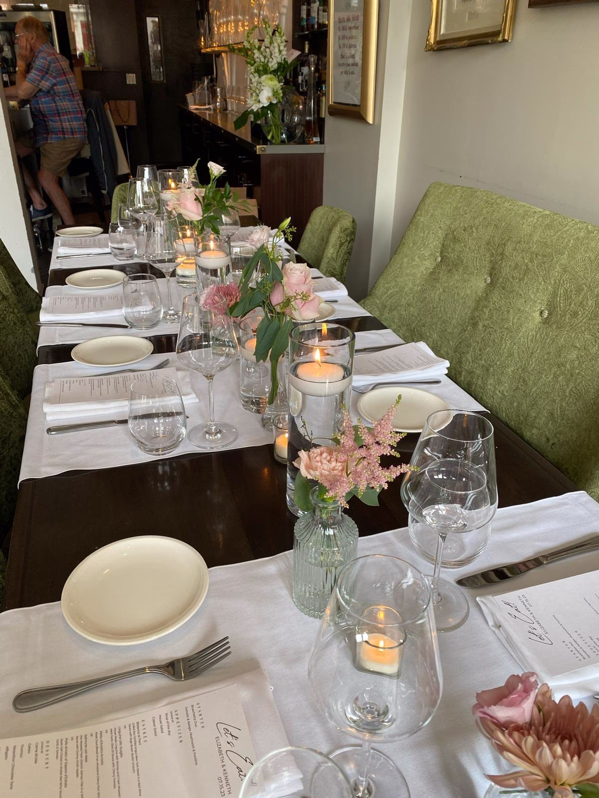 Intimate celebration dinner table set with petite bud vases of pink roses and astilbe and votive candles