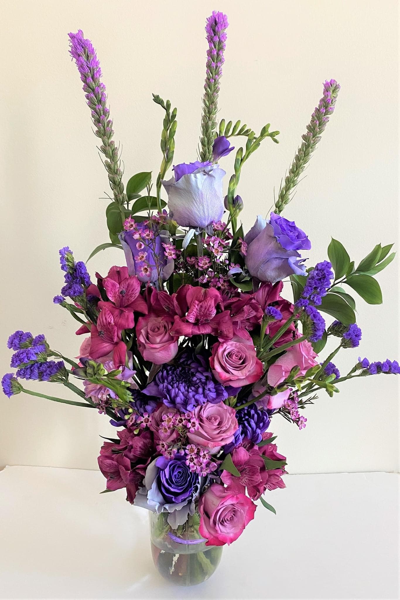 Blooms in Style arrangement of purple and lilac roses with liatris, statice, and freesia in a clear glass vase