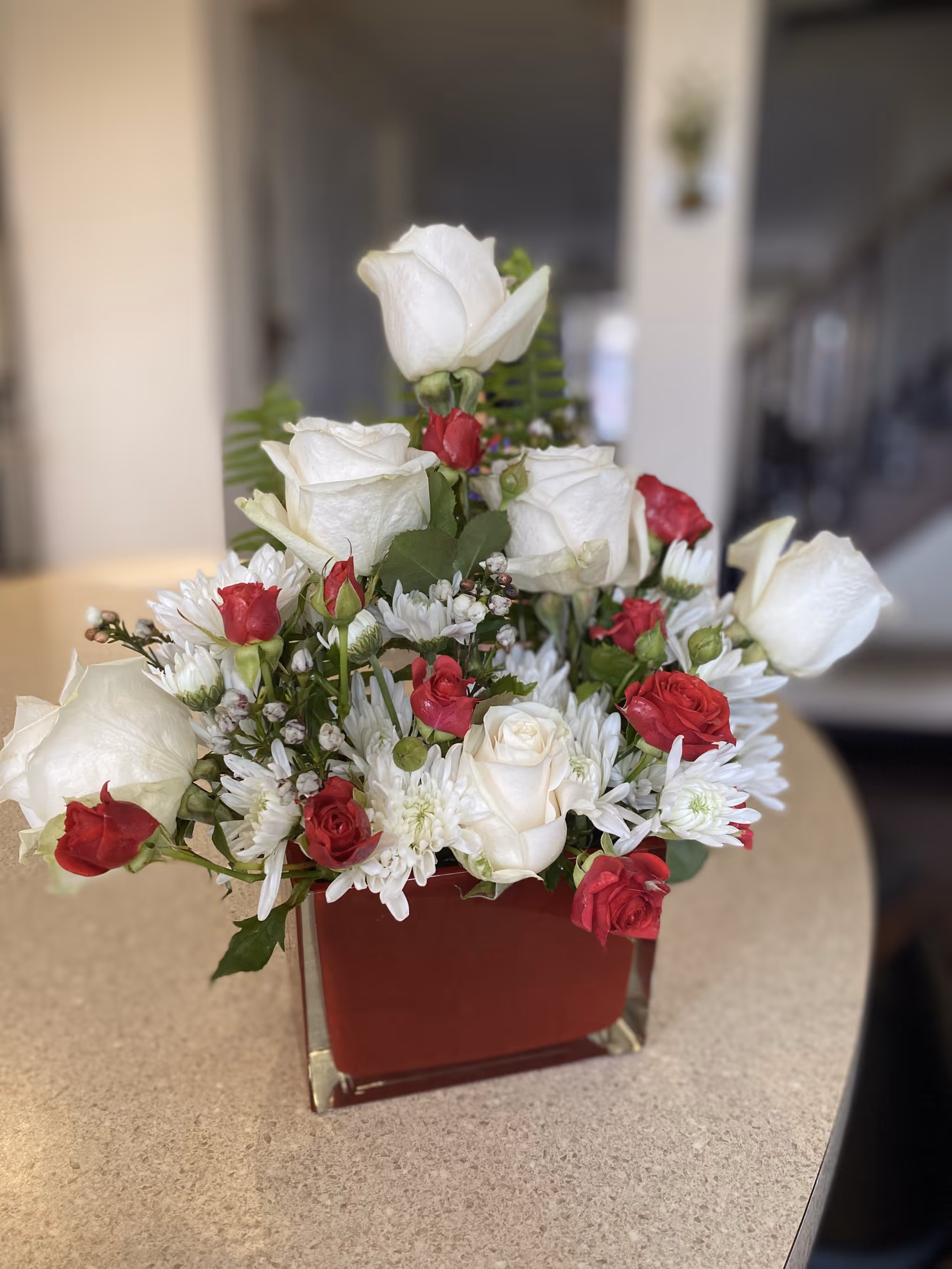 White roses and white chrysanthemums accented with red spray roses in a red cube vase