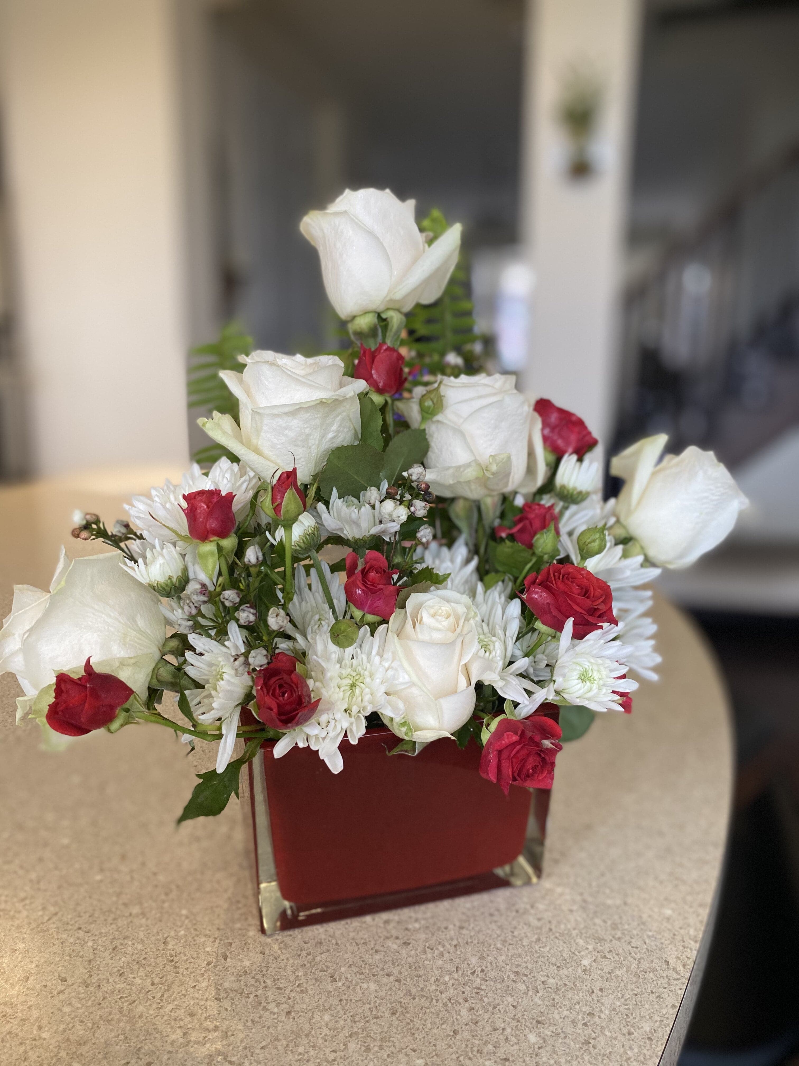 White roses and white chrysanthemums accented with red spray roses in a red cube vase