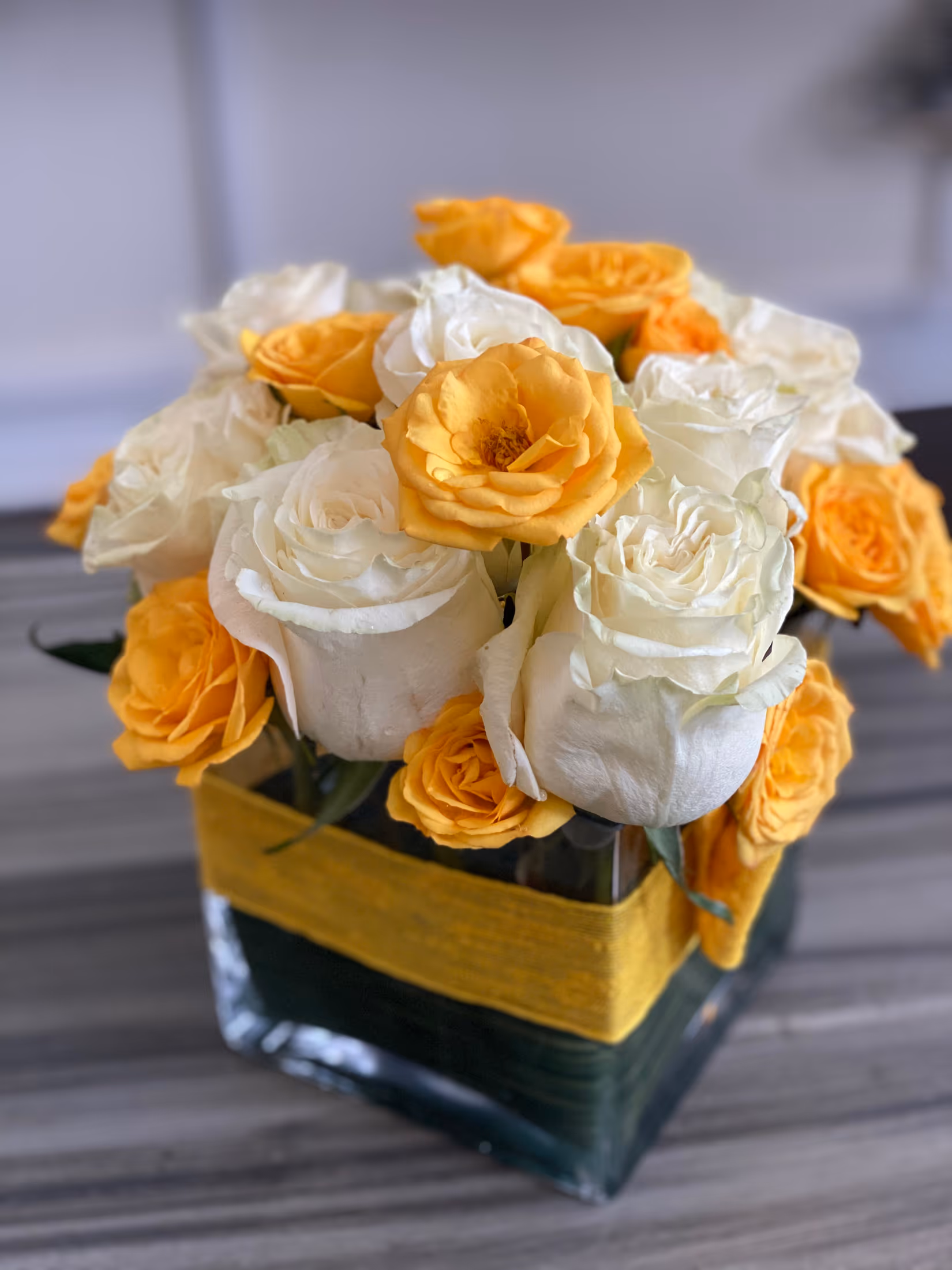Cube vase of white roses and yellow spray roses wrapped with a leaf and yellow band