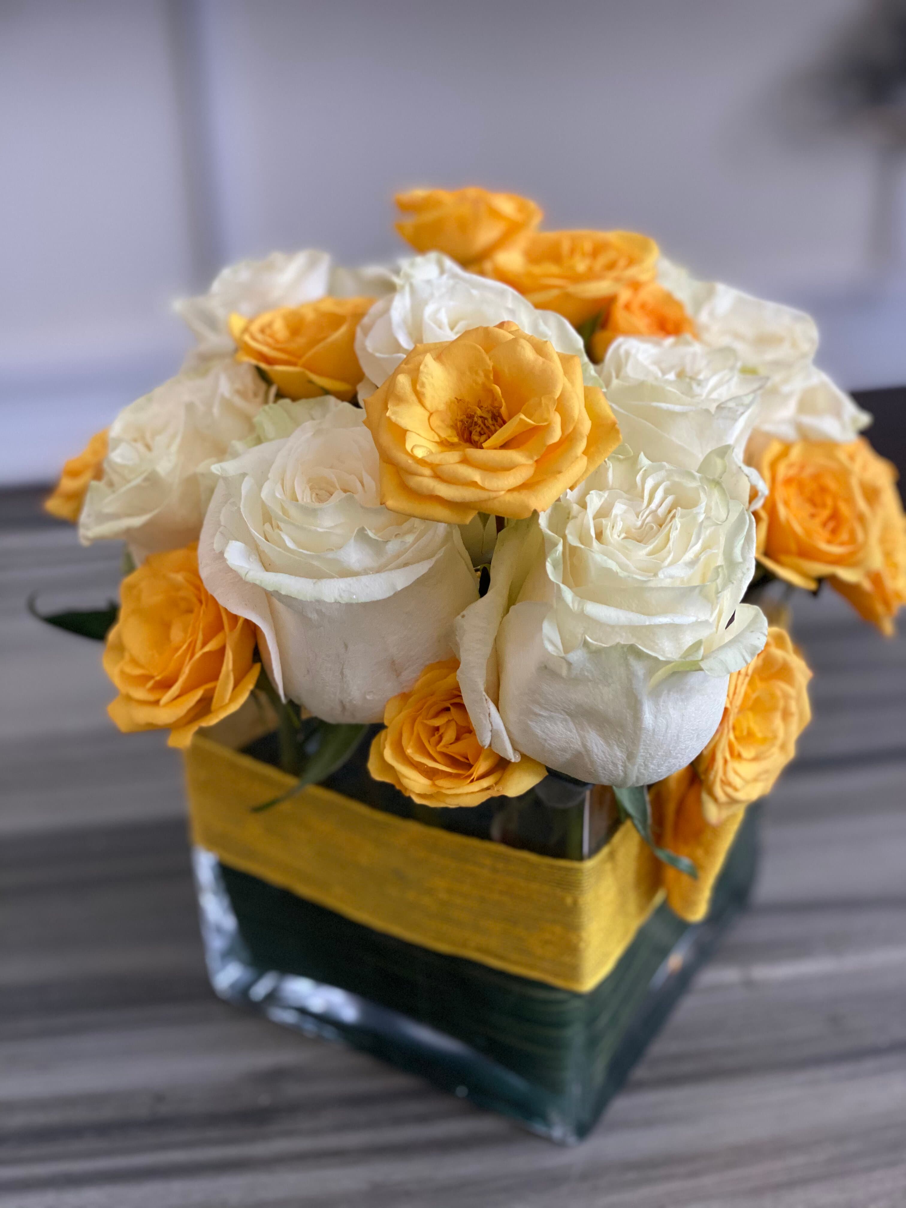 Cube vase of white roses and yellow spray roses wrapped with a leaf and yellow band