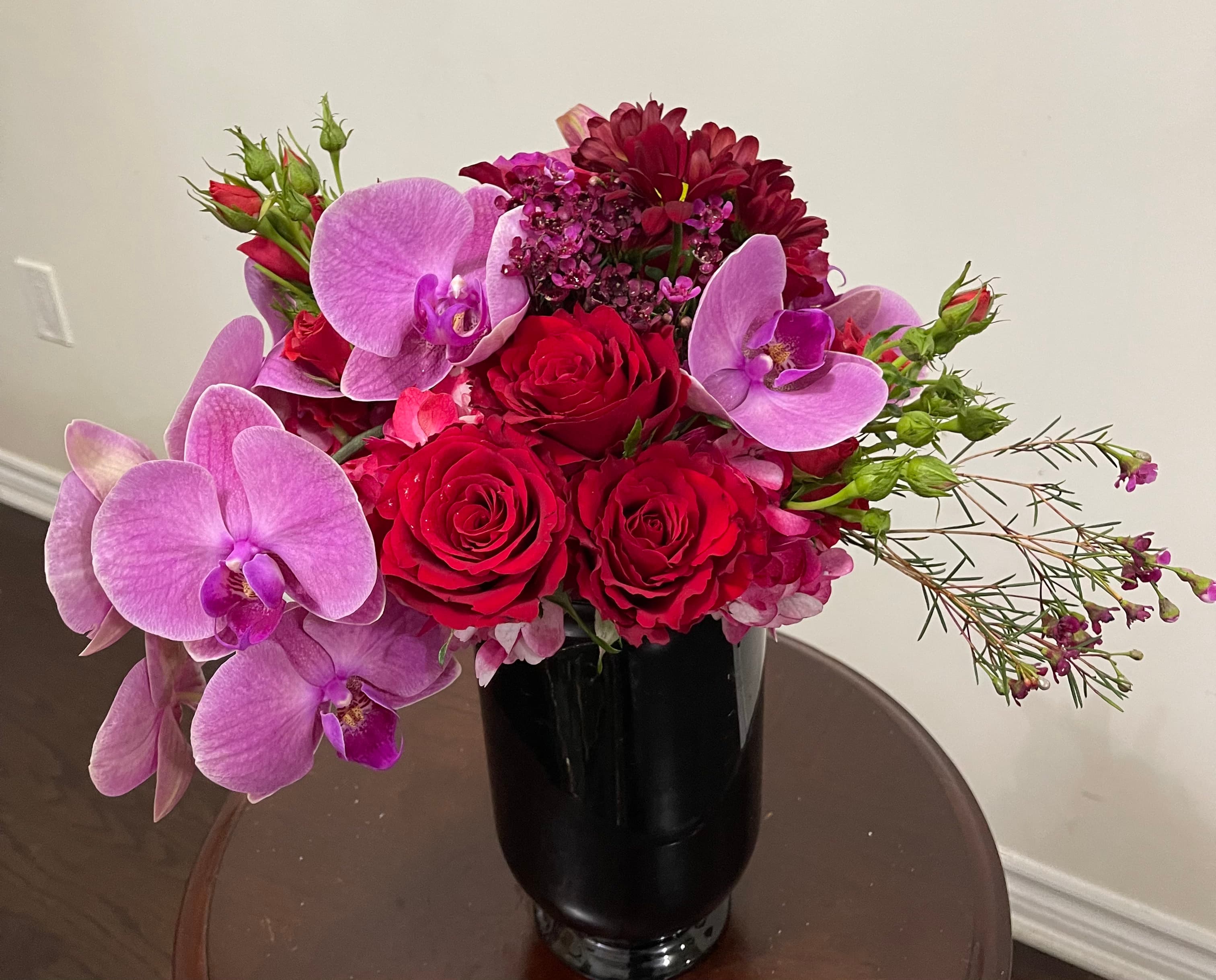 Pink Rainforest floral arrangement with pink orchids, hydrangeas, red roses, and spray roses in a black vase