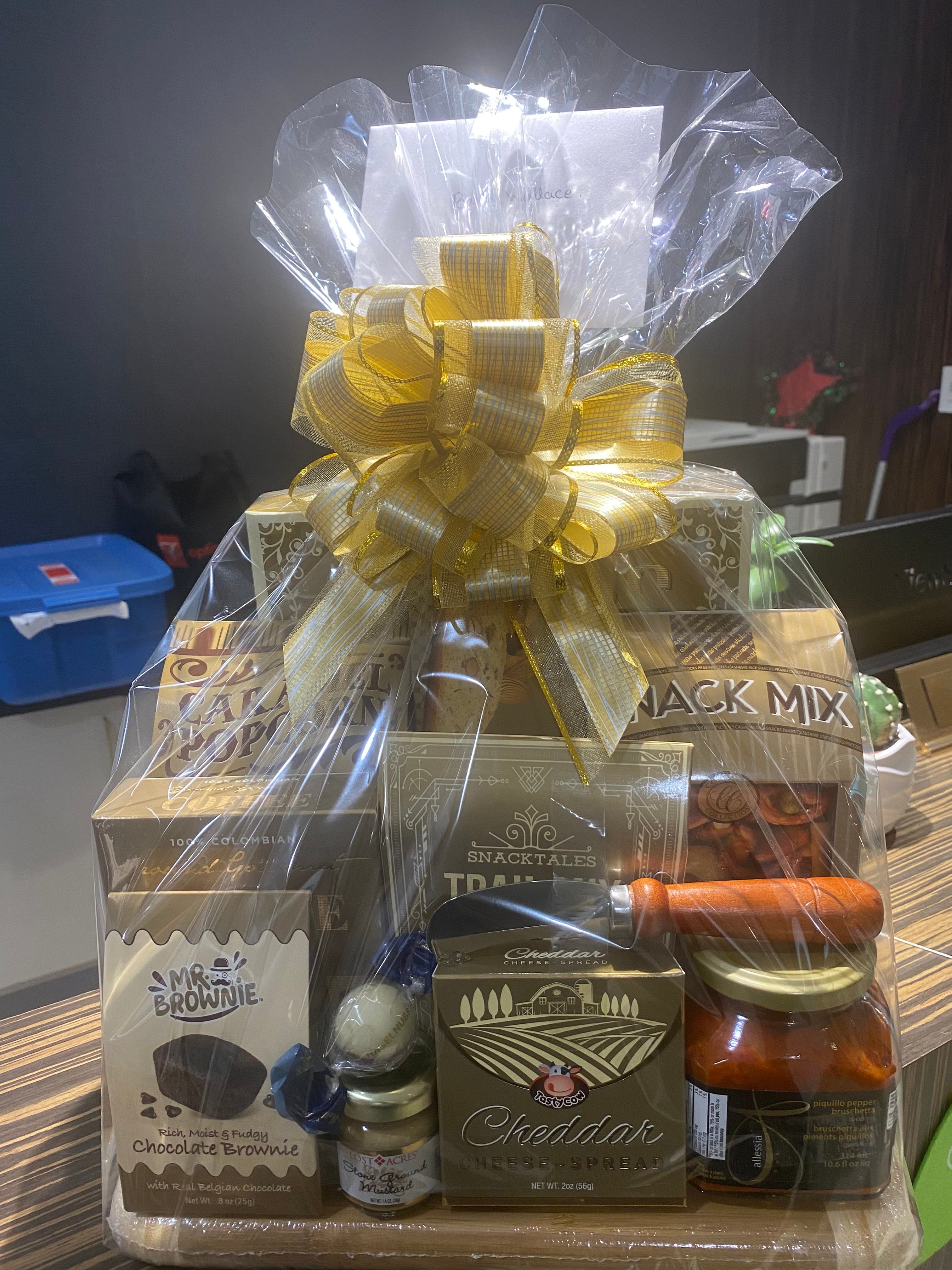 Gourmet gift hamper of snacks, chocolates, and preserves on a board, wrapped in cellophane with a gold bow