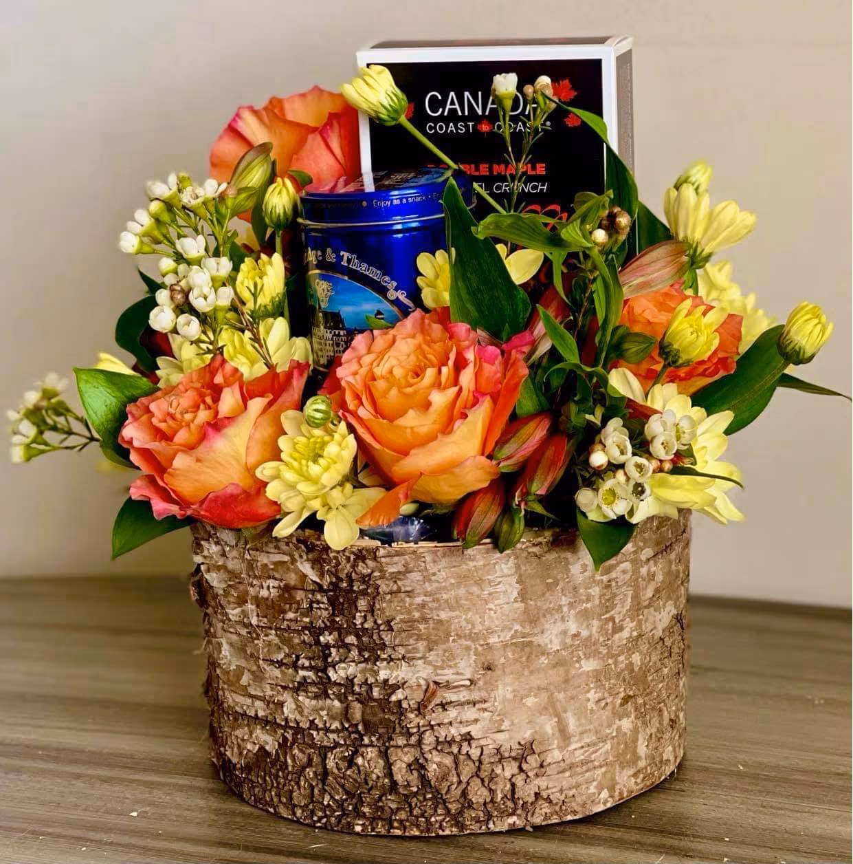 Birch-bark container of orange roses, alstroemeria, and waxflower with a tea tin and maple cookie boxes