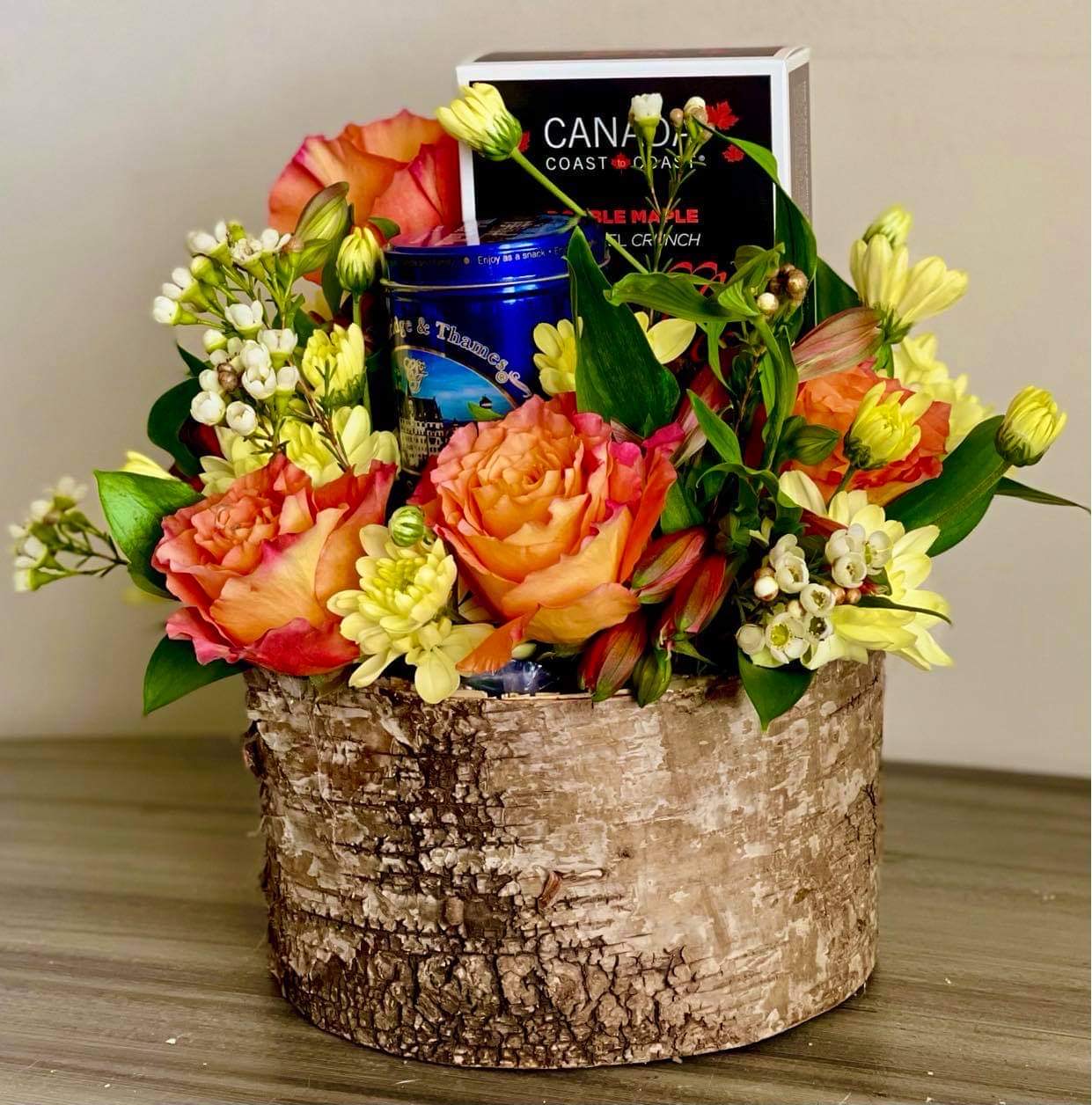 Birch-bark container of orange roses, alstroemeria, and waxflower with a tea tin and maple cookie boxes