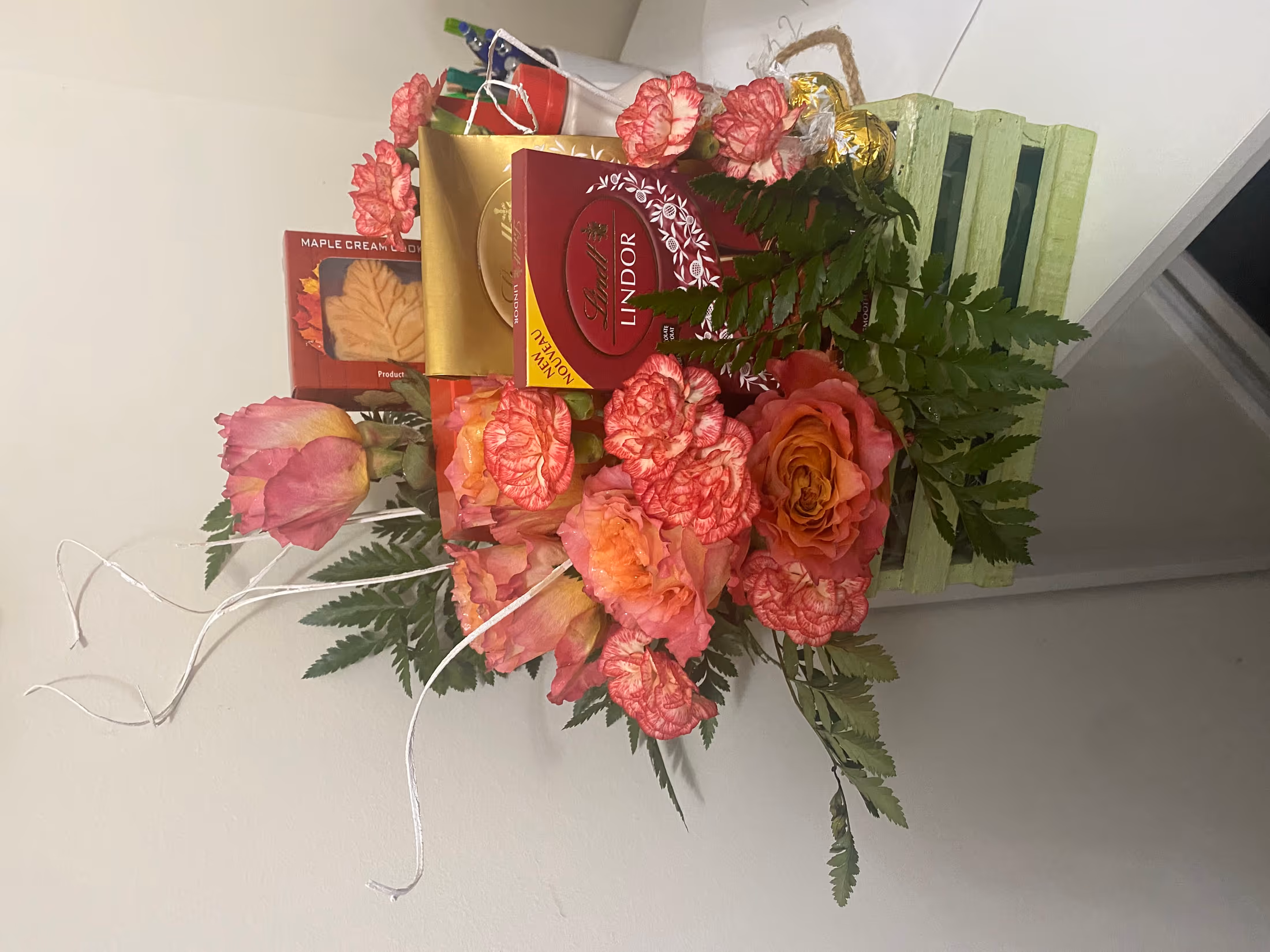 Peach carnations and roses with ferns beside boxed Lindt chocolates and maple cream cookies