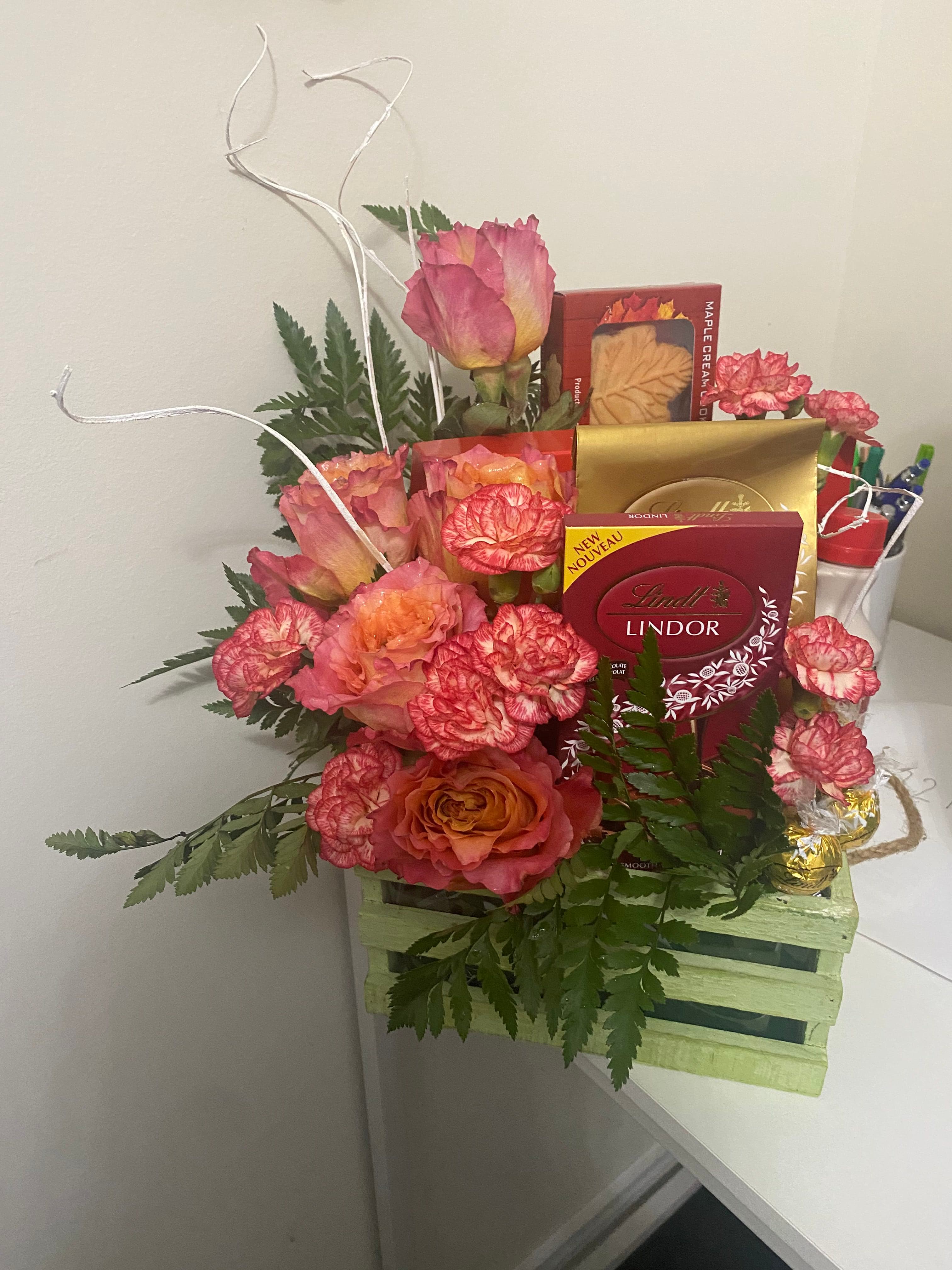 Peach carnations and roses with ferns beside boxed Lindt chocolates and maple cream cookies