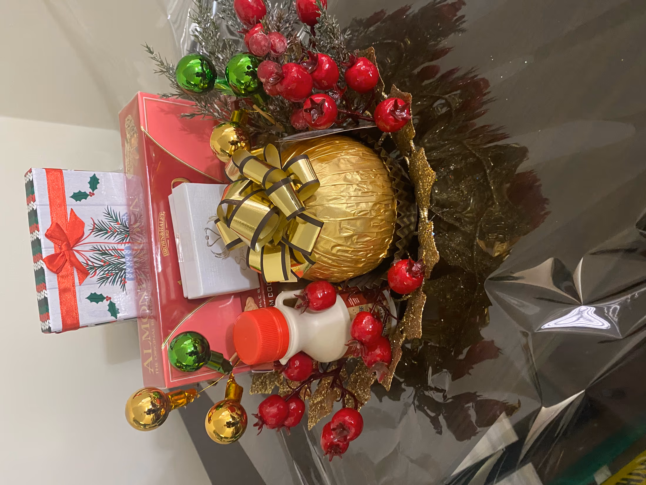 Holiday gift display with a gold bow, red berries, ornaments, and boxed cookies on a decorative gold plate