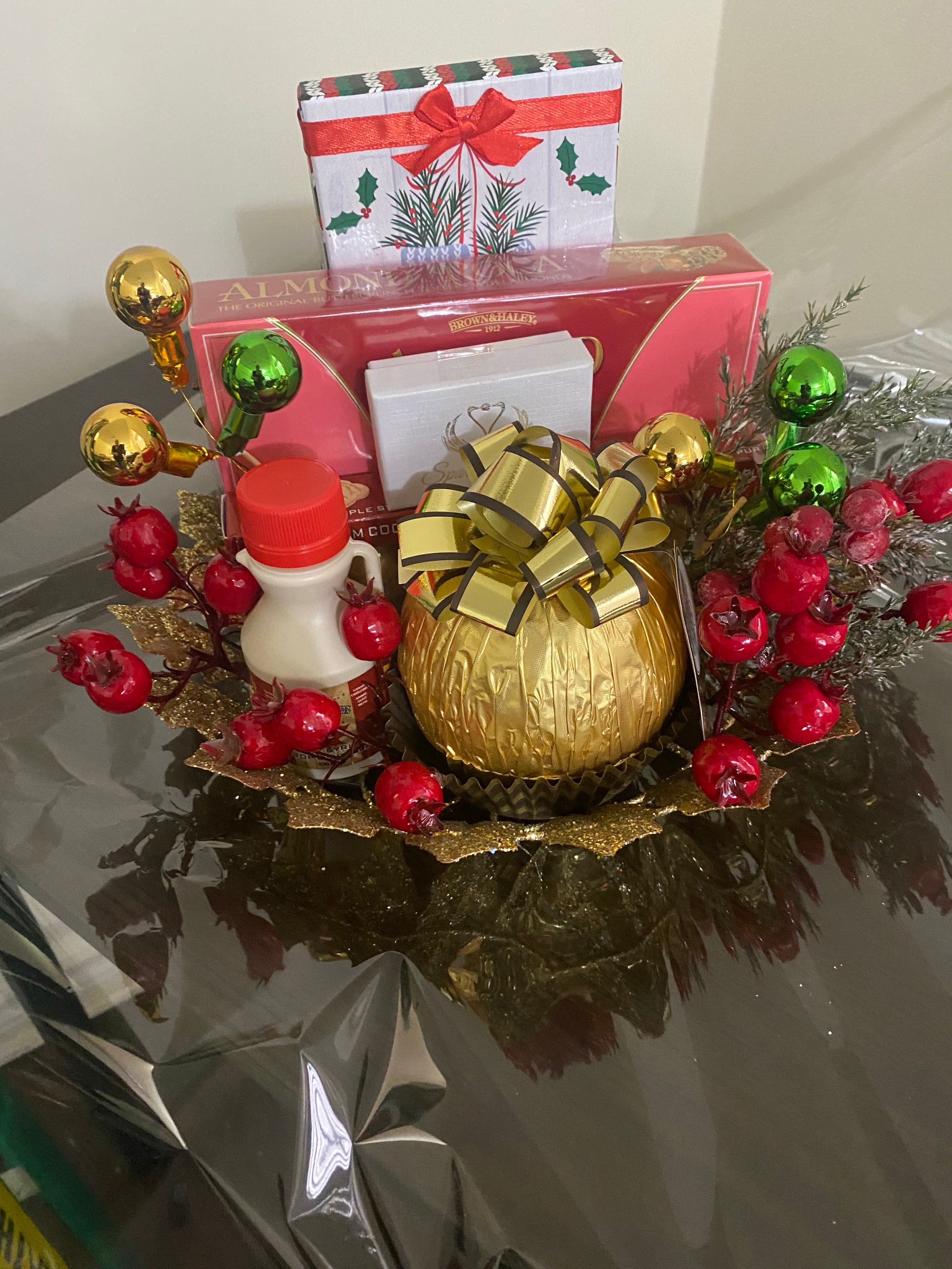 Holiday gift display with a gold bow, red berries, ornaments, and boxed cookies on a decorative gold plate