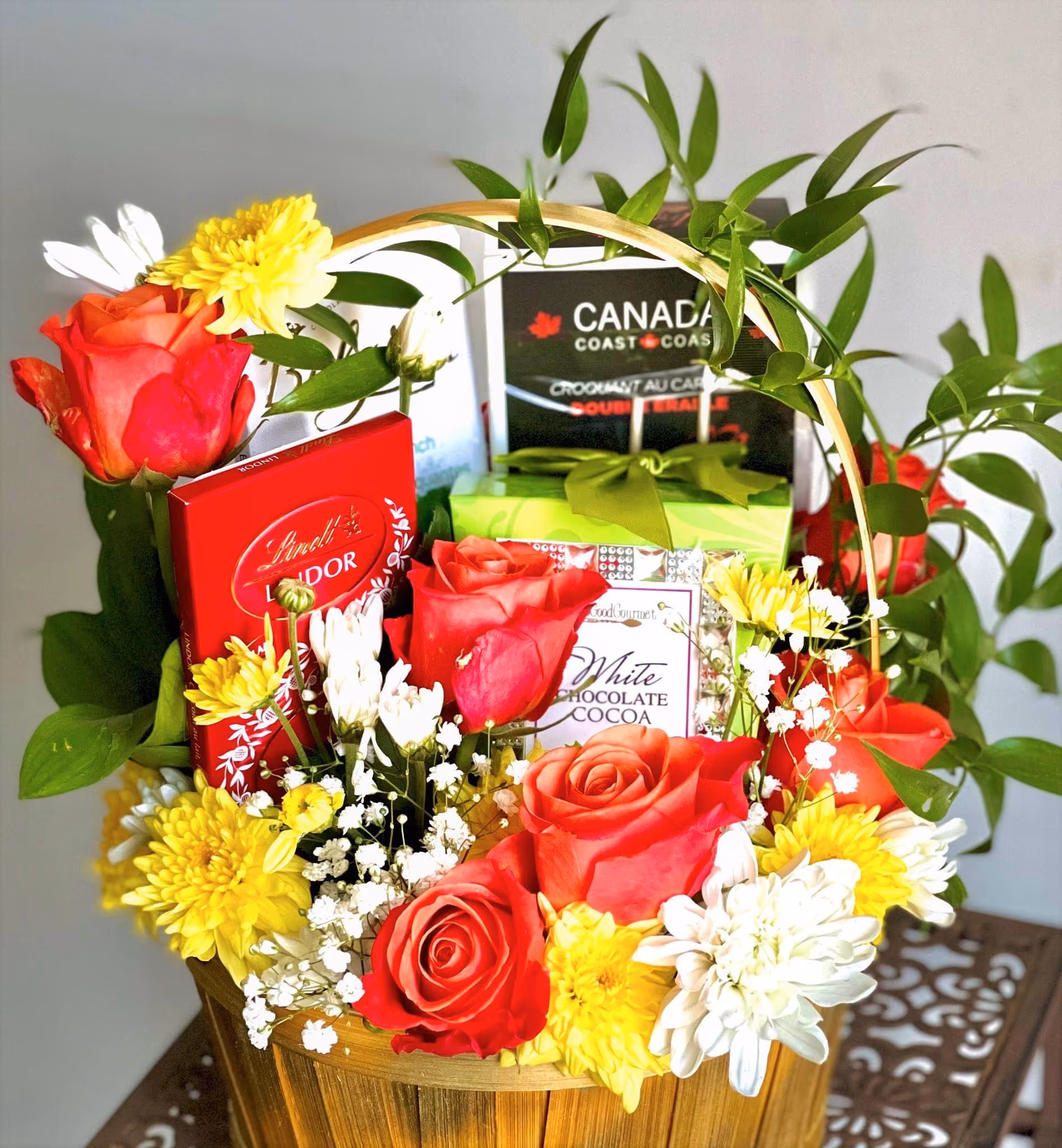 Willow basket of orange roses, yellow mums, and white daisies with boxed chocolates and cocoa