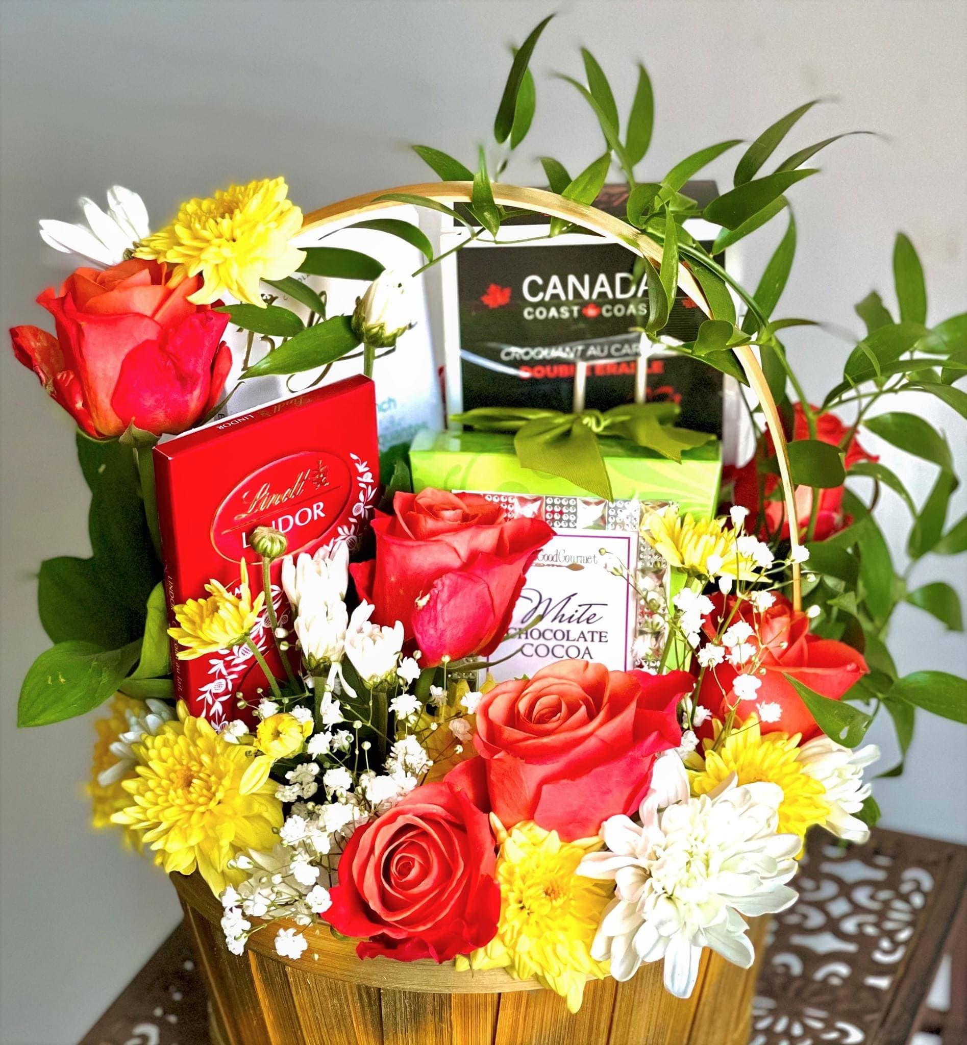 Willow basket of orange roses, yellow mums, and white daisies with boxed chocolates and cocoa