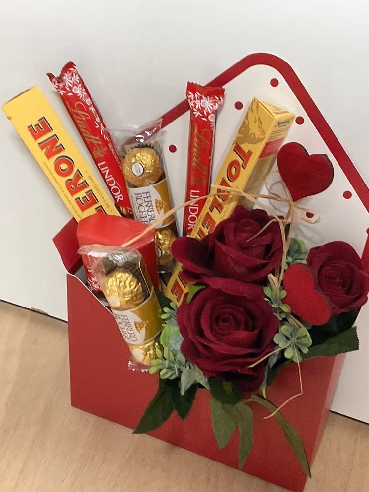Red envelope-style box filled with red roses, Toblerone, Lindt, and Ferrero Rocher chocolates with a heart accent