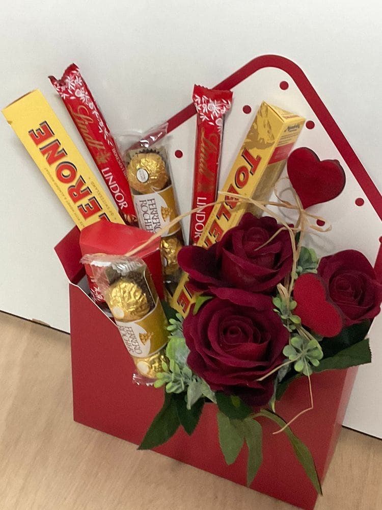 Red envelope-style box filled with red roses, Toblerone, Lindt, and Ferrero Rocher chocolates with a heart accent