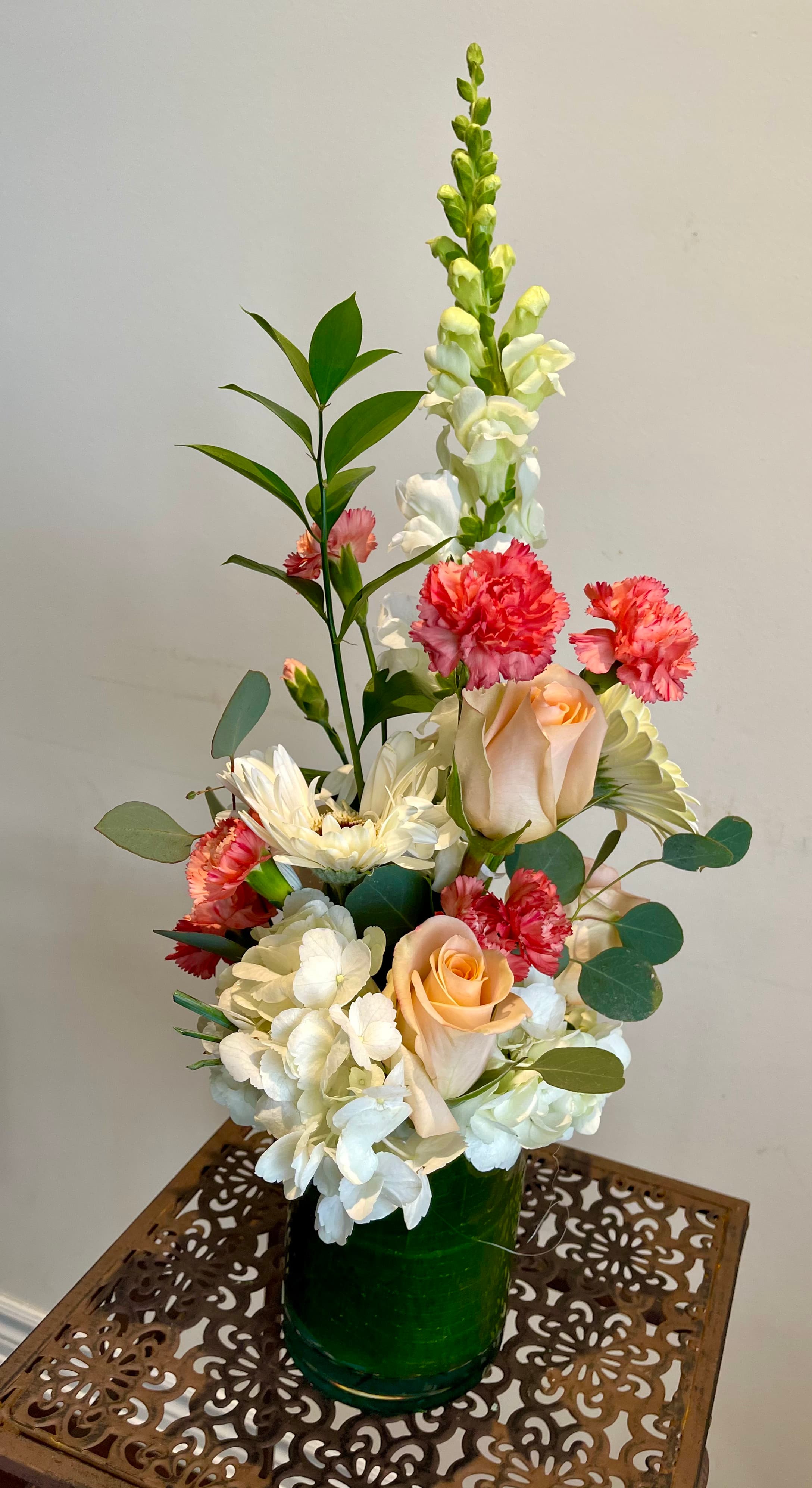 Summer Fresh arrangement of peach roses, coral carnations, white hydrangea, and snapdragons in a leaf-lined glass vase