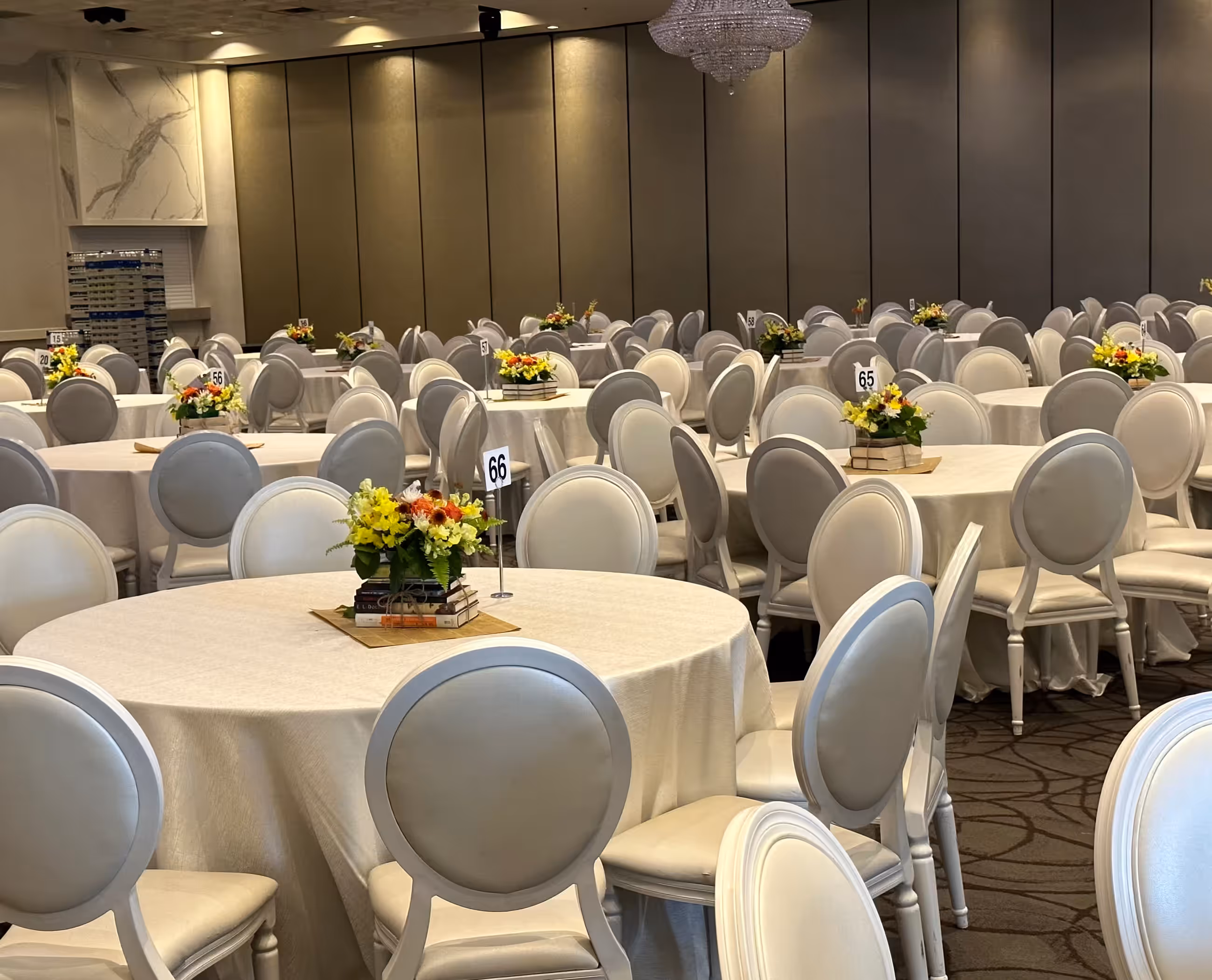 A ballroom set with round tables, matching chair covers and small floral centerpieces for a formal seated reception