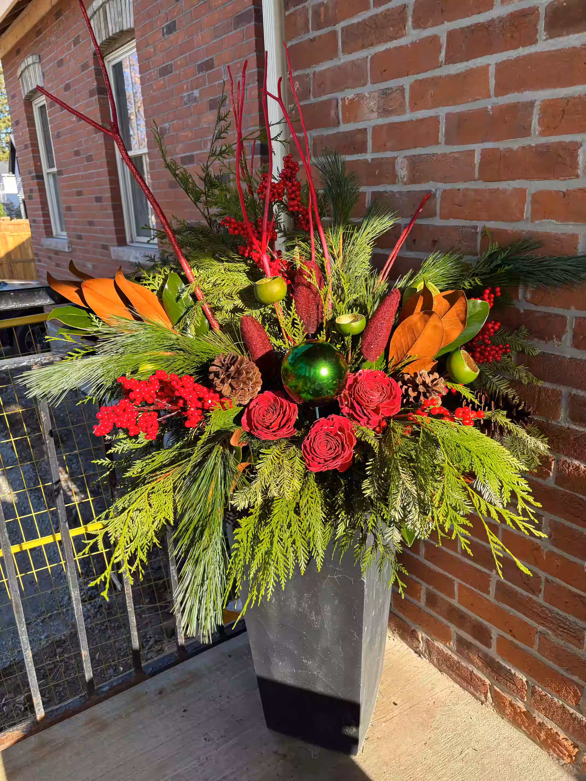 A red and green holiday urn arrangement with roses, pinecones and magnolia leaves on a porch
