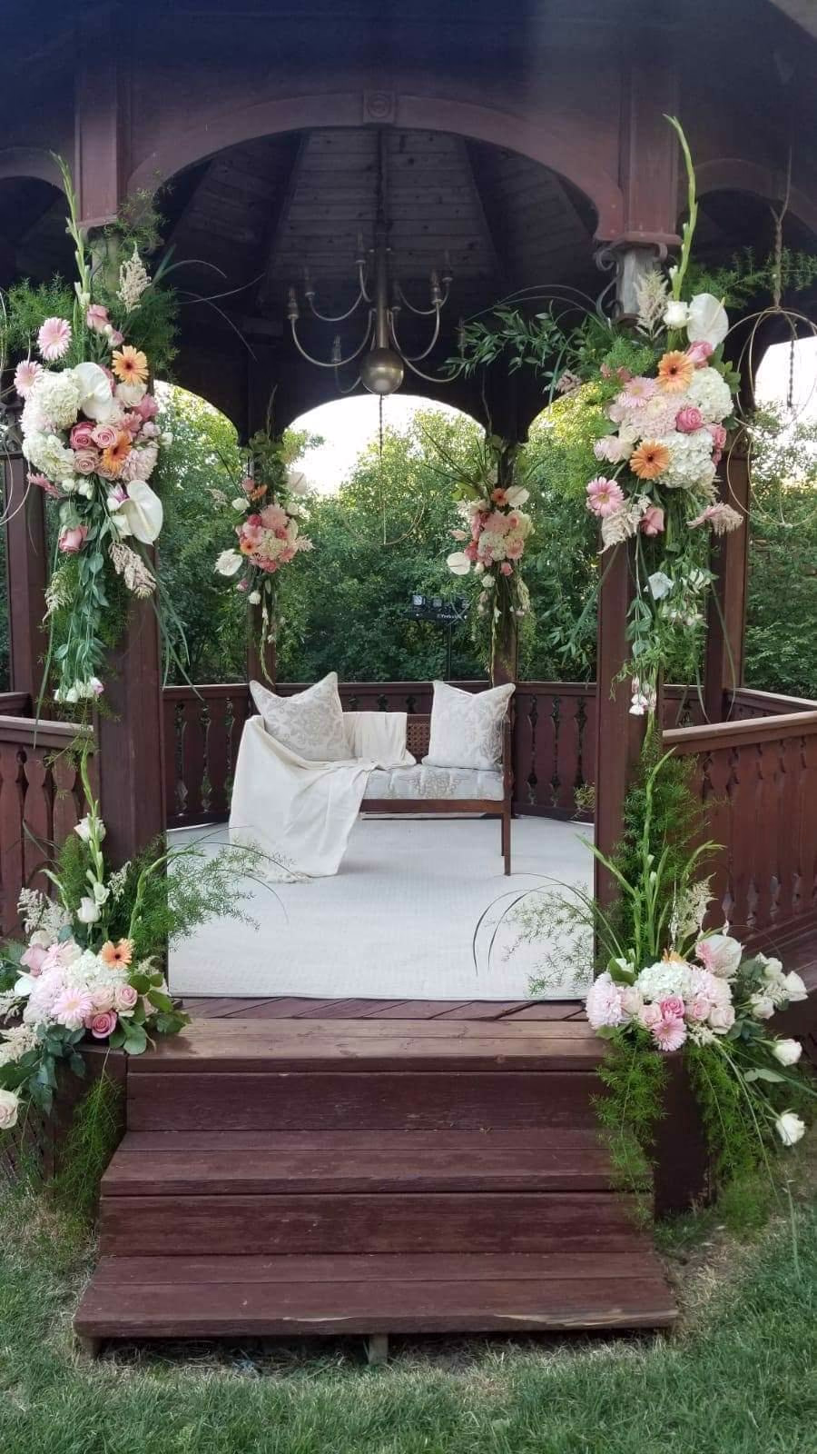 Wooden gazebo ceremony setting framed with blush and peach floral arrangements