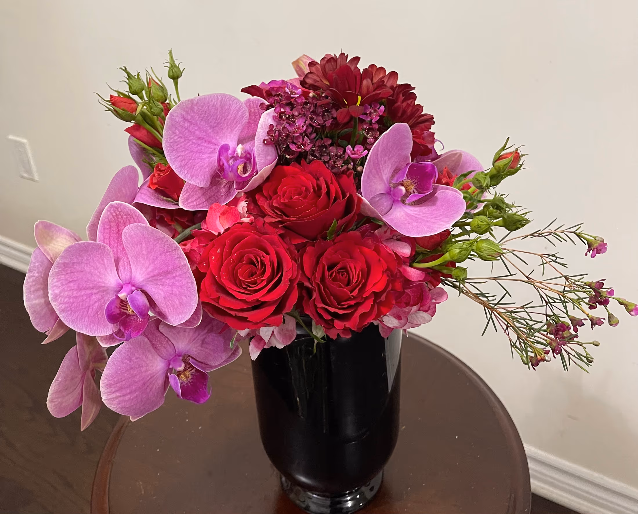 Pink Rainforest floral arrangement with pink orchids, hydrangeas, red roses, and spray roses in a black vase